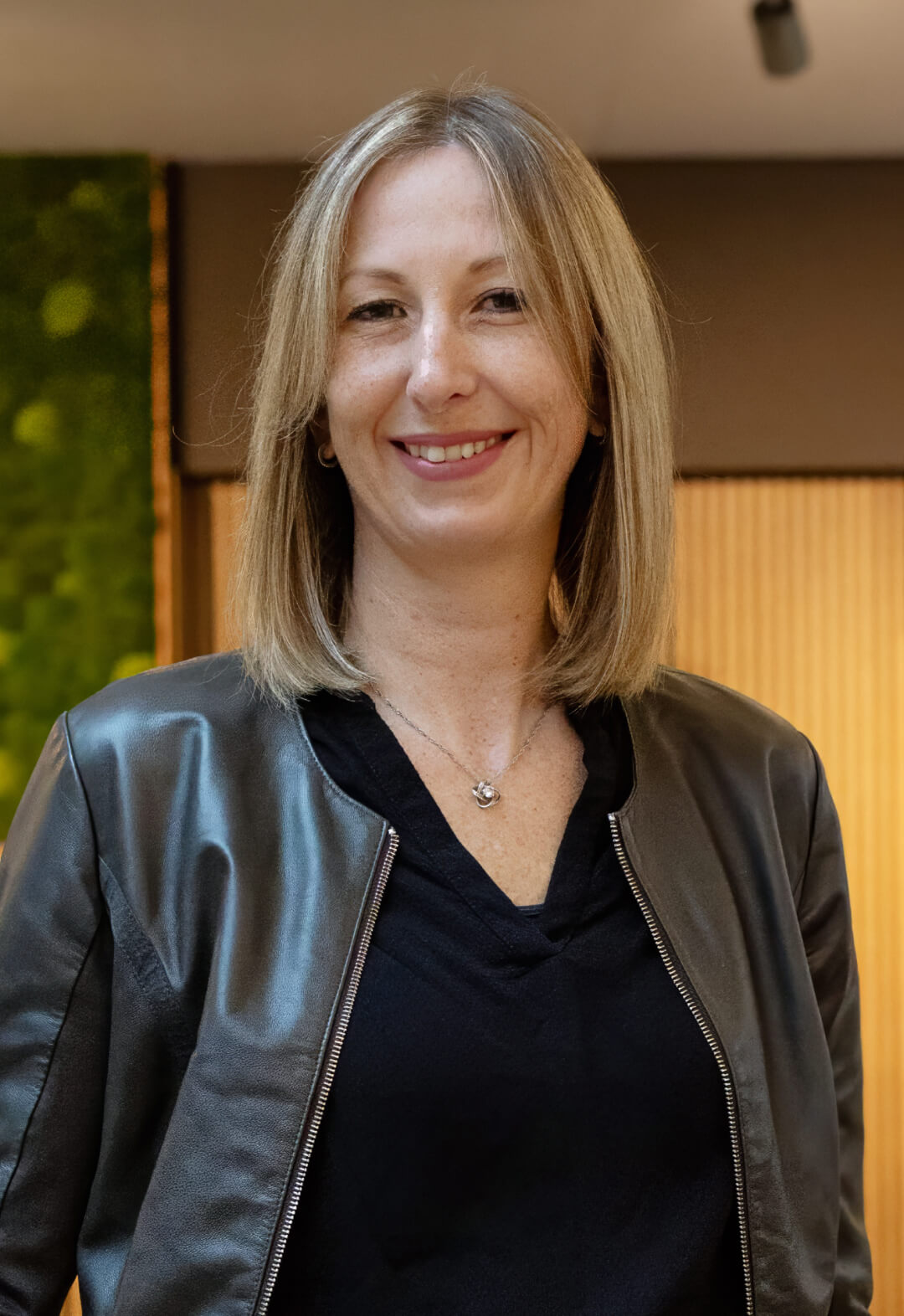 Frau mit blondem Haar und Lederjacke lächelnd in heller Umgebung