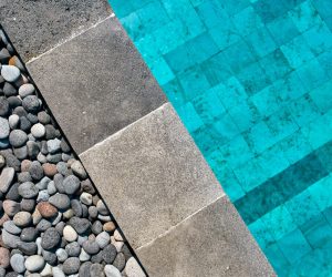 Nahaufnahme von dunklen Natursteinfliesen im Poolbereich neben Kieselsteinen