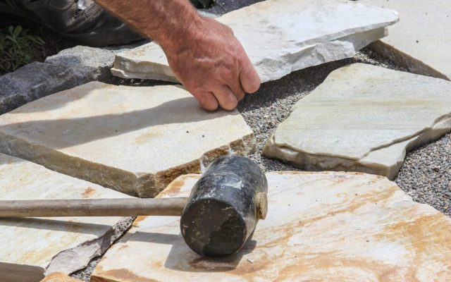 Handwerker legt Natursteinplatten mit Gummihammer und Werkzeug