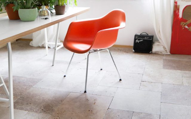 Moderner Raum mit orangefarbenem Designerstuhl auf Steinfliesen