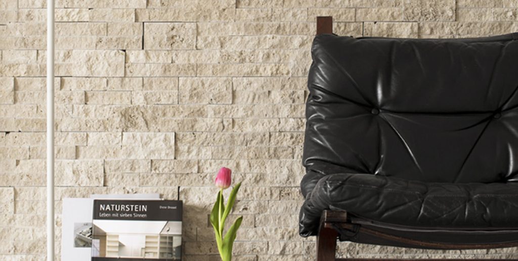 Natursteinwand in hellem Beige mit schwarzem Ledersessel und Vase