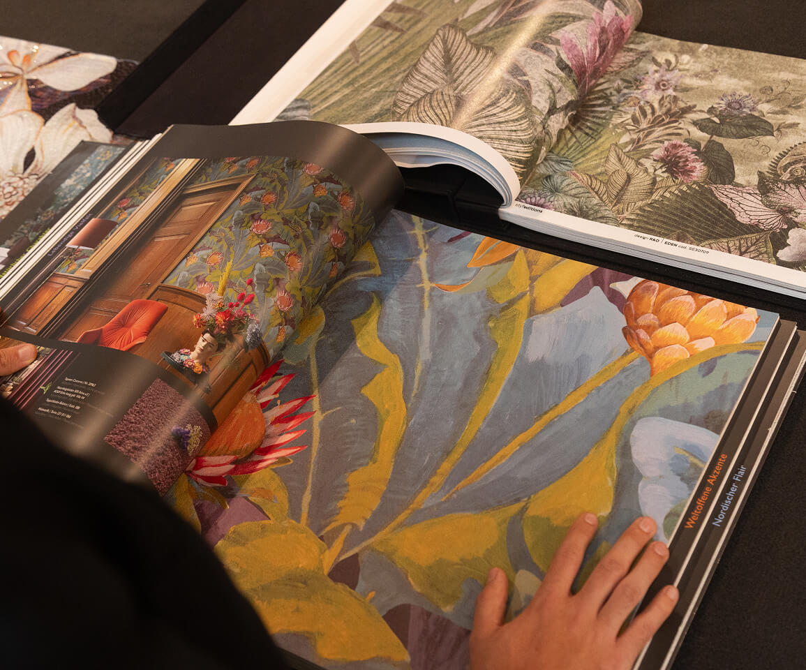 Person blättert durch ein Musterbuch mit farbenfrohen Tapetendesigns