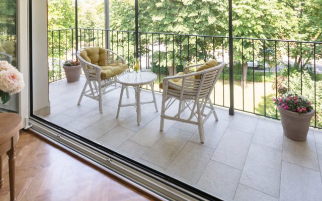 Balkonterrasse mit zwei Korbstühlen und rundem Tisch, umgeben von grünen Bäumen