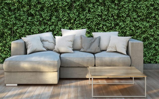 Modernes Wohnzimmer mit hellem Sofa vor grüner Pflanzenwand